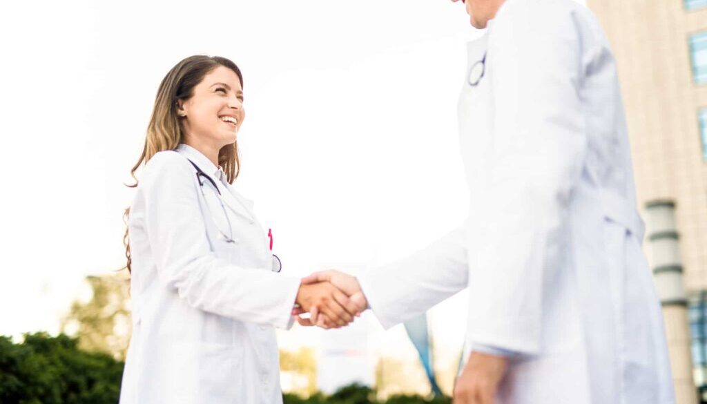 Young female healthcare worker shaking hands with doctor. Bringing on a New Provider? The Importance of Not Waiting For Credentialing