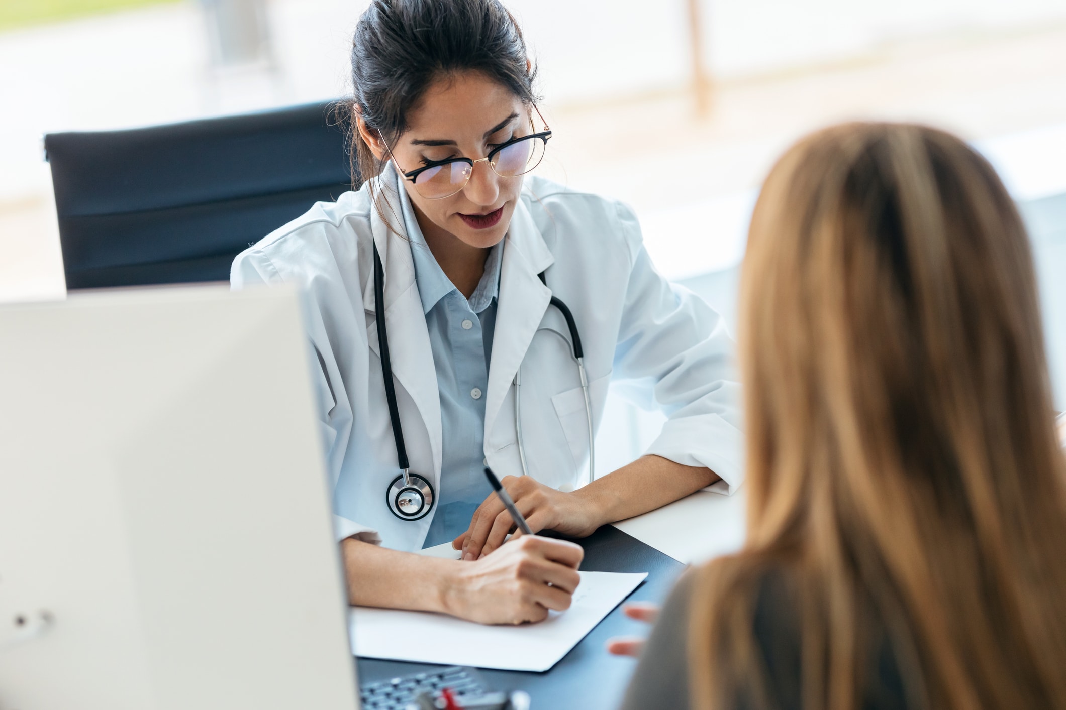 Beautiful cheerful female doctor talking while explaining medical treatment to patient in the consultation.