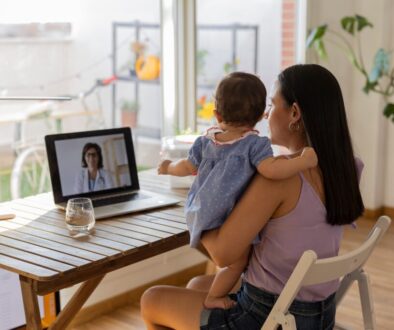 mother on her back with her daughter in her arms sitting on a video call with the doctor - virtual appointment, medicine at home